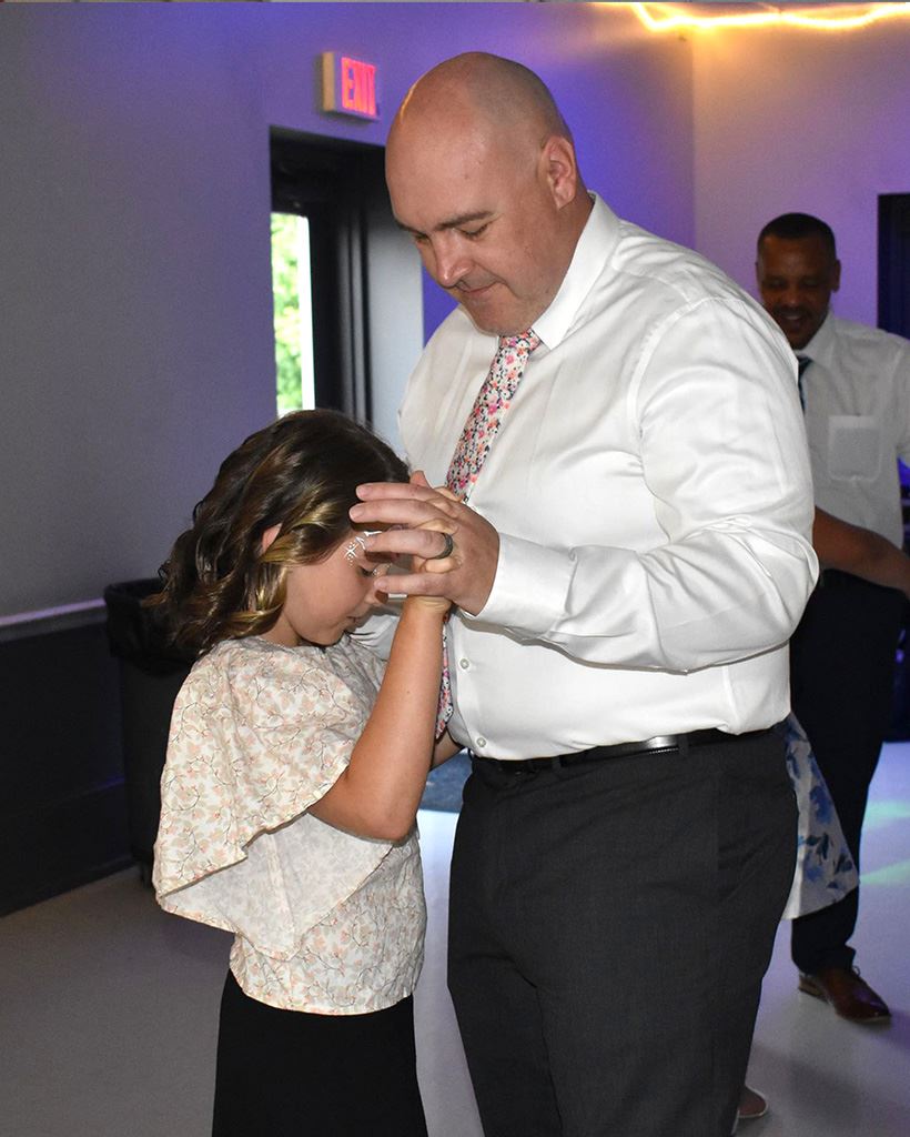 A father and daughter in dress attire dancing.